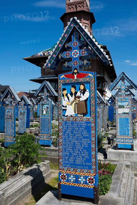 Tomb depicting people in traditional clothing surrounded by ornate tombs, traditional wooden grave sites, Happy Cemetery, Cimitirul Vesel, Sapân?a, Sapanta, Maramure?, Maramures, Maramures, Maramures, Romania