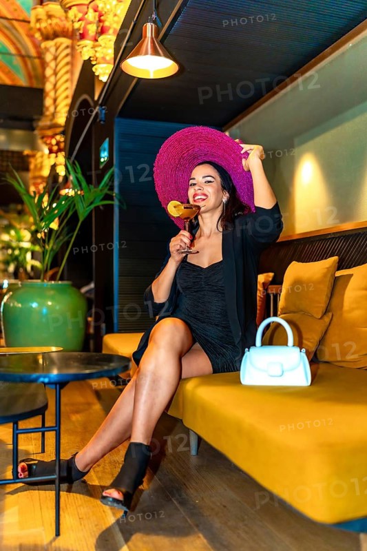 Vertical photo of a stylish and elegant woman on a cocktail bar enjoying sitting alone and drinking