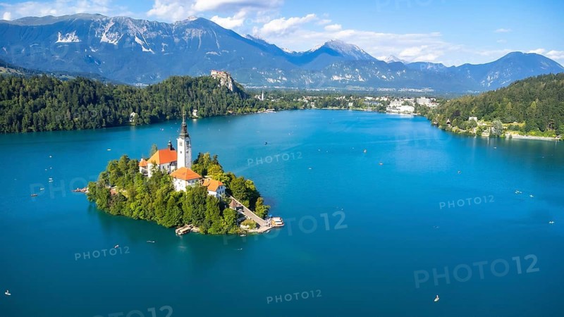 Aerial view of lake bled featuring the assumption of mary church on a small island, with kayakers enjoying summer in the julian alps