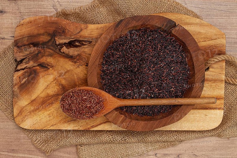 Red and black rice, in a wooden bowl and spoon on a wooden surface in rustic style, top view