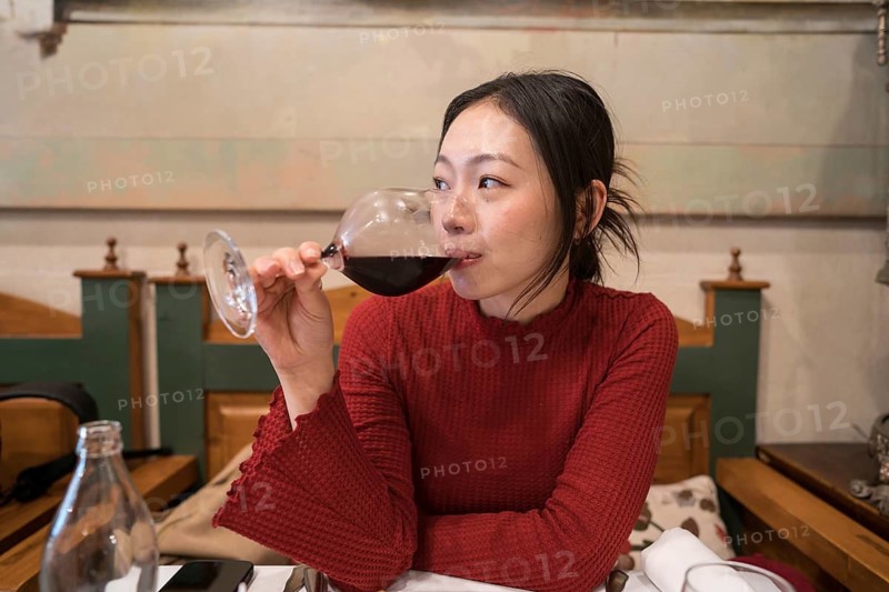 An asian female tourist savors a glass of red wine in Segovia, Spain. Her relaxed demeanor and elegant surroundings capture the essence of leisure and cultural exploration