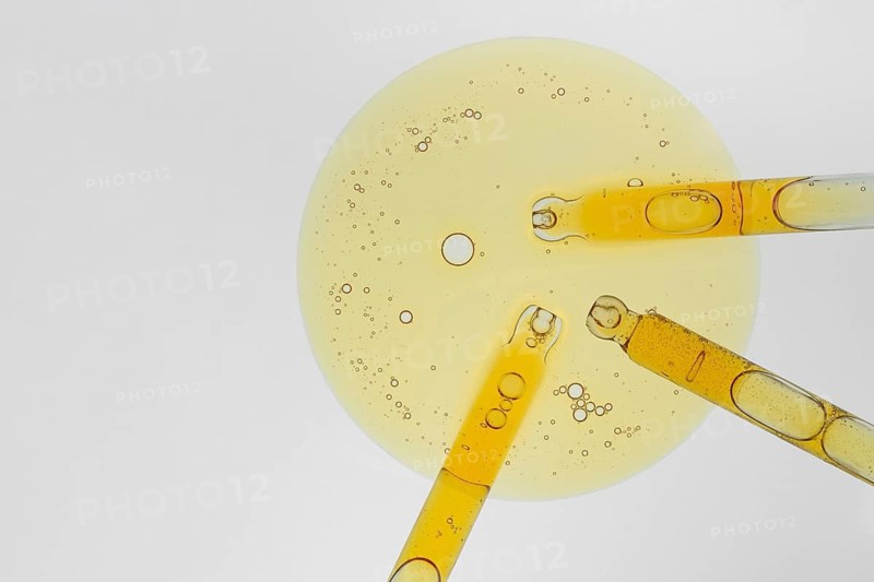 A close up image of three pipettes filled with yellow liquid placed on a petri dish. Bubbles in the liquid create an intricate pattern of textures. Perfect for cosmetic and medical concepts