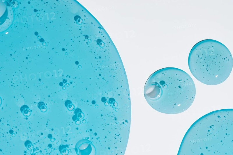 Close-up shot of blue cosmetic gel droplets with intricate texture on a white background. The image highlights the translucent quality and bubble details of the gel