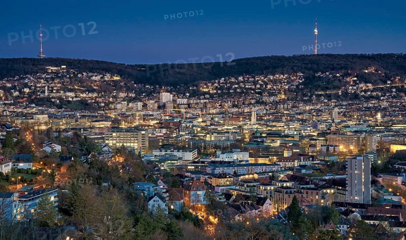 Panoramic night view of Stuttgart city center in Germany with glowing city lights, dense urban architecture and residential hills. Television towers visible on the surrounding hills, Stuttgart, Baden-Wuerttemberg, Germany