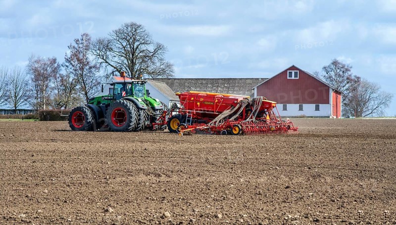 Farming, sowing with tractor in springtime and with a farm building in the background in Skurup municipality, Skåne county, Sweden, Scandinavia
