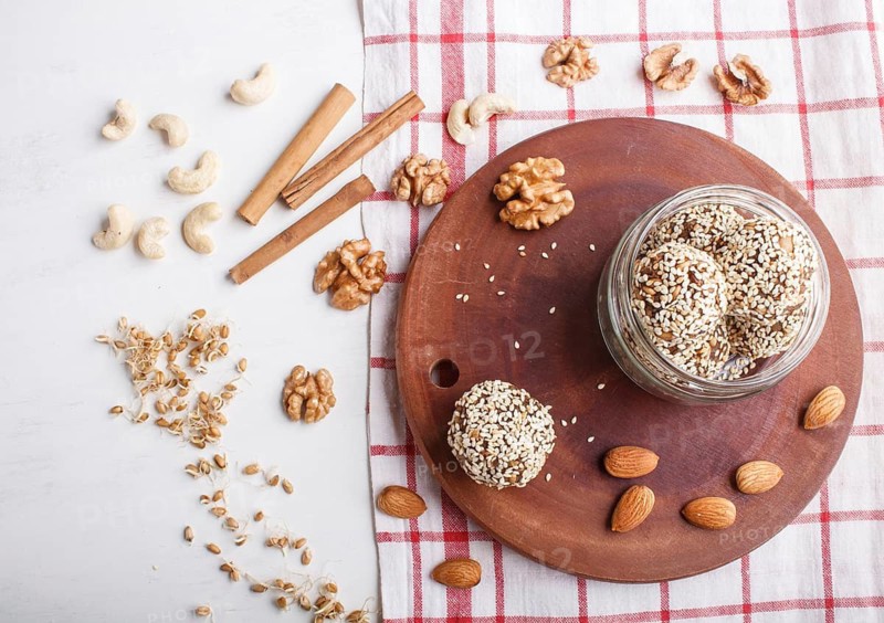 Energy balls cakes with almonds, sesame, cashew, walnuts, dates and germinated wheat on wooden board in glass jar, top view, close up