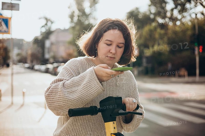 A woman scans a QR code on an electric scooter using her smartphone for easy rental in a sunny urban setting