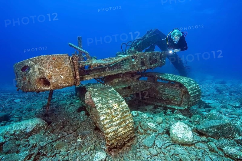 Diver looks at illuminated for diver sunken wreck of excavator tracked vehicle, Tenerife, Canary Islands, Spain
