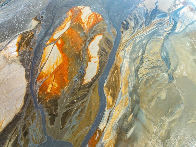 Top view abstract of a winding river cutting through sandy textures, revealing a stunning fusion of amber, gold, and gray hues. The drone shot image captures the ethereal beauty of nature's artistry from above