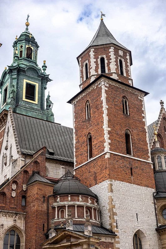 Krakow, Poland, 23.08.2025: Historic architecture in Krakow, Poland. Features a brick tower with a conical roof and green copper dome. Cloudy sky in the background