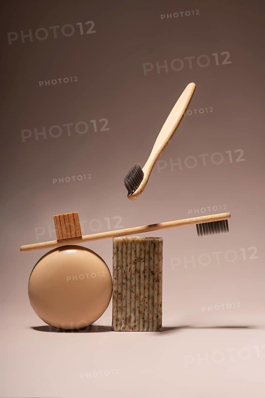 Aesthetic arrangement of bamboo toothbrushes balanced on natural soap and a round beige object, set against a soft brown background. Eco-friendly, zero waste concept