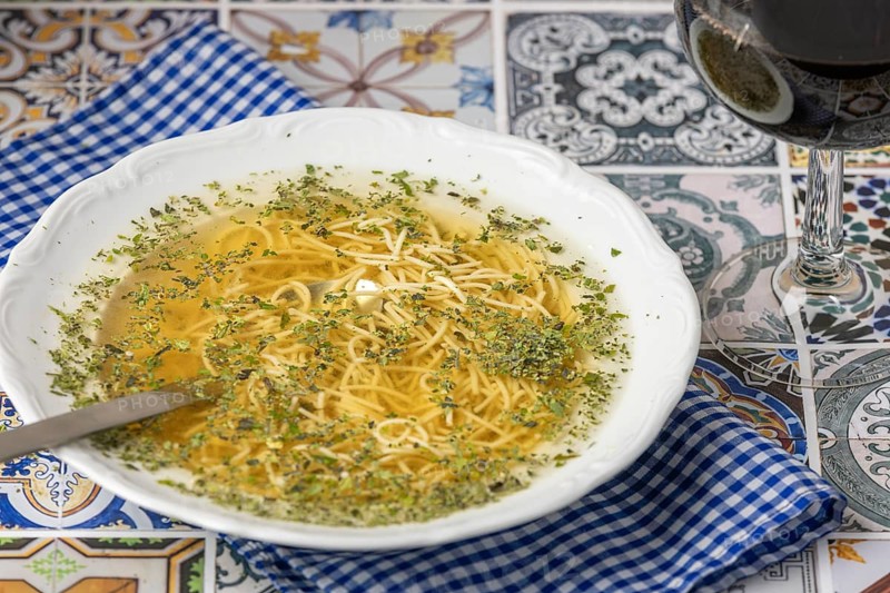 Noodle soup with herbs in a white plate next to a glass of red wine