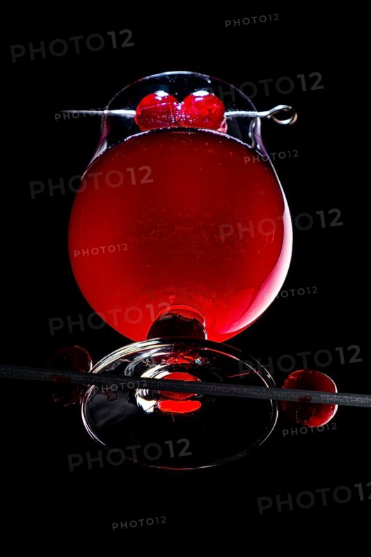 A cognac glass with red liquid and cherries, dramatically illuminated, view from below