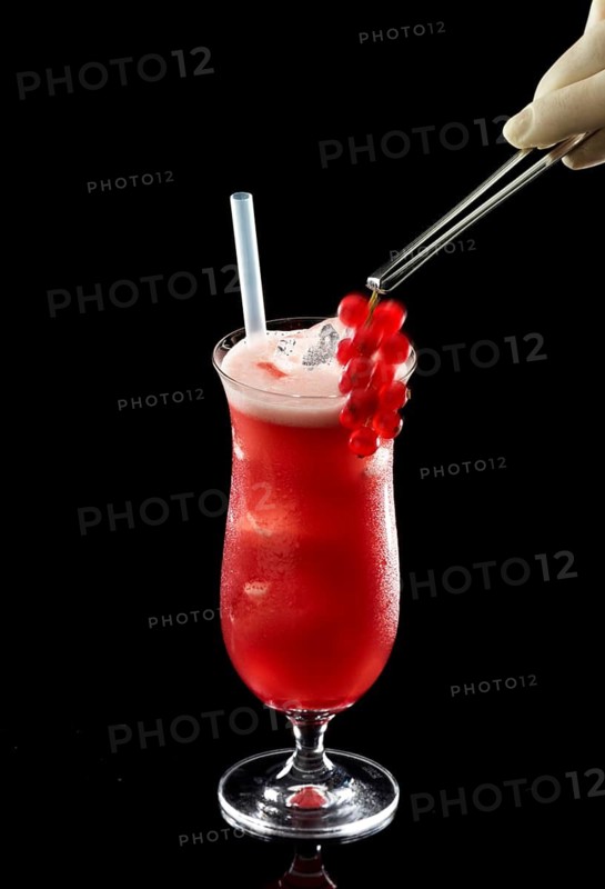 Red cocktail on ice cube cubes against a black background, red currants as garnish, studio recording