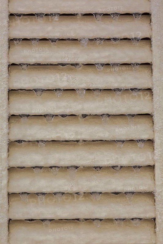 Close-up of icicles hanging from tan coloured angled slats on decorative tan colored louver panel in late winter, Quebec, Canada
