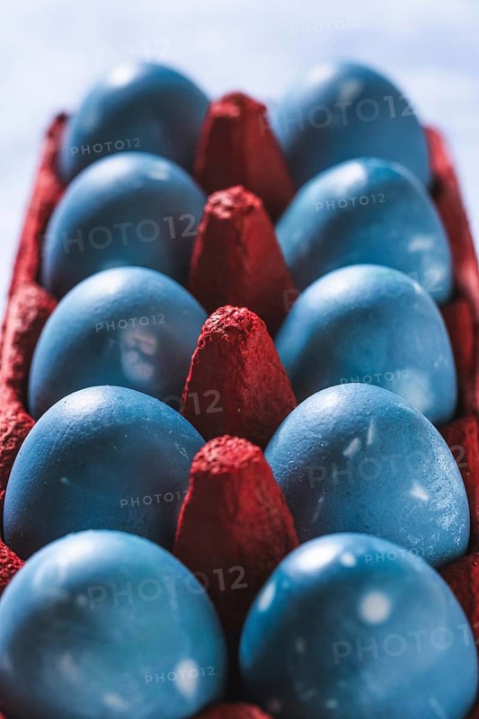 Vibrant blue Easter eggs neatly arranged in a bold red egg carton, shot from above. The contrasting colors create a striking visual