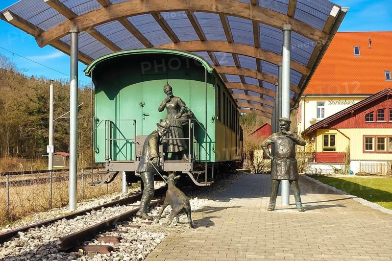 Durlesbach railway station, opened in 1849 and decommissioned in 1984, railway monument, railway memorial, group of figures by the artist René Auer, group of sculptures, scene from the song Auf de schwäbische Eisebahne, billy goat, woman, farmer, conductor, s Bäuerle, Konduktör, s Weible, bronze figures, Königlich Württembergischen Staats-Eisenbahnen, station building at the back right, Durlesbach, Reute, Bad forest lake, Upper Swabia, Baden-Württemberg, Germany