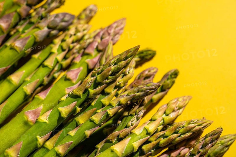 Close-up of fresh green asparagus spears set on a vibrant yellow background, highlighting their natural textures and colors. Perfect for healthy food and cuisine-related designs