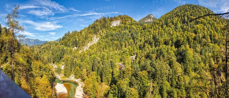 An expansive mountain panorama with densely wooded slopes under a clear blue sky, Klobenstein