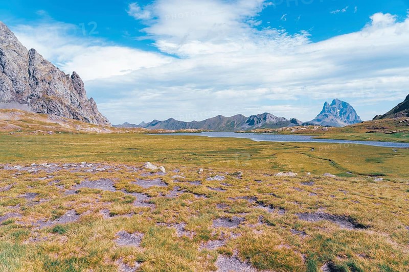 Scenic view of the lush, open landscapes at Ibones de Anayet in Huesca, Spain. The vibrant green meadows and tranquil waters set against a dramatic backdrop of rugged mountain peaks create a breathtaking natural scenery
