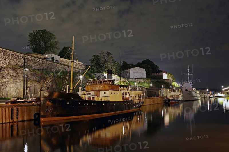 Illuminated ships in a quiet harbour at night with lights in the water, old fortress, Oslo, Norway