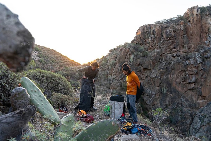 Climbers prepare their gear at sunset in a rugged natural landscape, surrounded by rocky cliffs and vegetation, embodying the spirit of adventure and nature