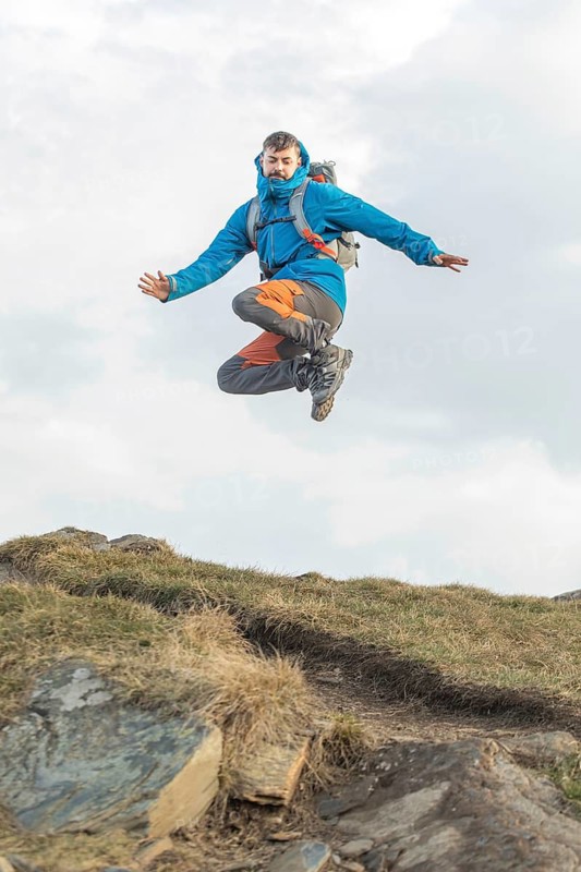 A man in vibrant outdoor gear joyfully leaps during a trekking adventure in the Pyrenees. The image captures the essence of exploration and freedom in the mountains