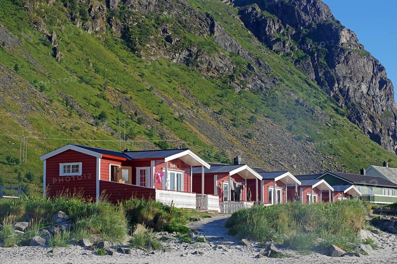 Red holiday cabins on the beach in front of green mountains on a sunny day, nature scenery, Ramberg, Flakstad, Lofoten, Nordland, Norway