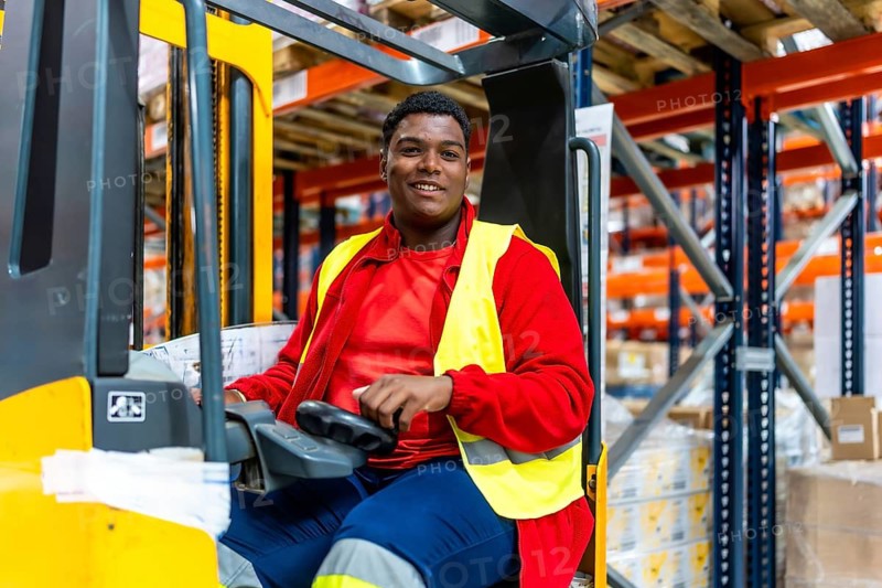 Happy young latin man driving forklift in a distribution warehouse