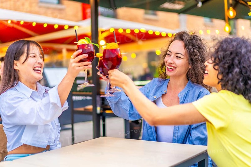 Three multi-ethnic women toasting with cocktails a sidewalk bar