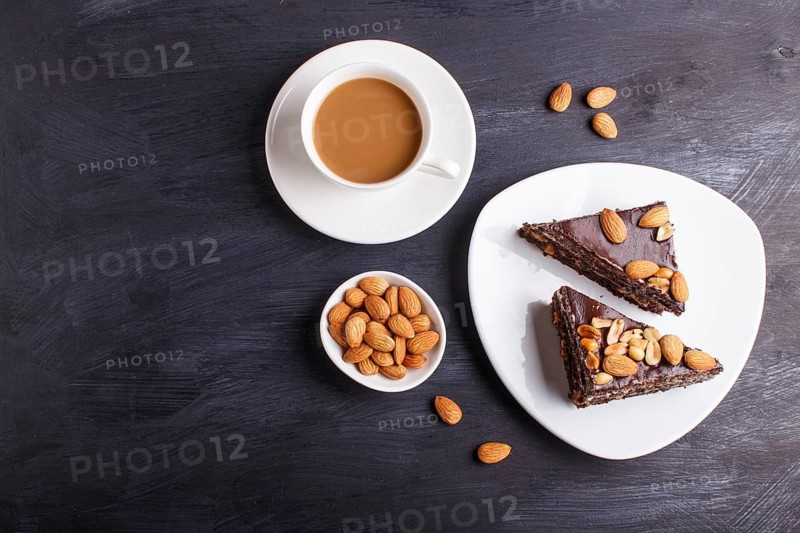 Chocolate cake with caramel, peanuts and almonds on a black wooden background. cup of coffee, top view, copy space