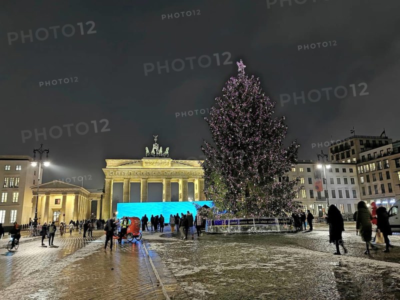 Nocturnal scene at Brandenburg Gate with illuminated Christmas tree and people, Berlin