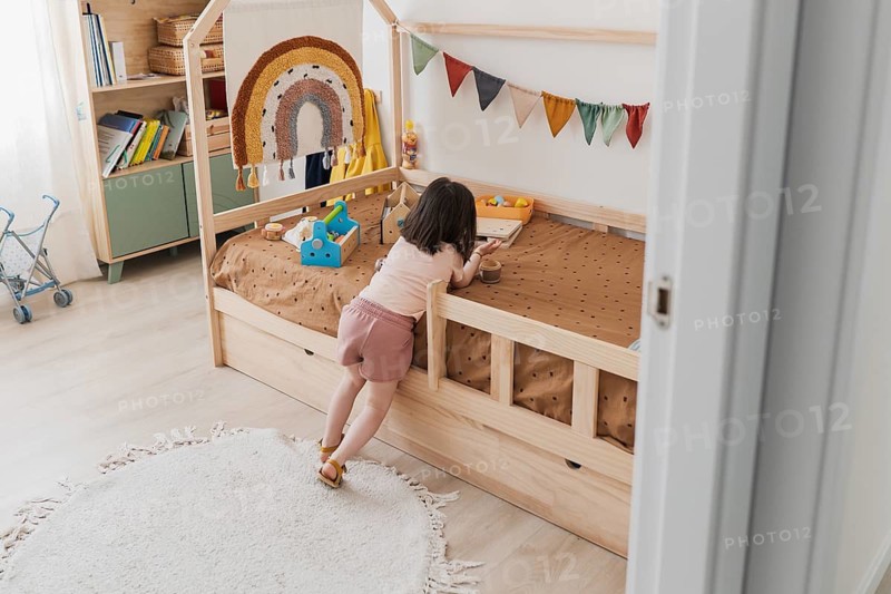 A young girl plays in a cozy, colorful bedroom with a wooden bed and playful decorations, highlighting a child-friendly and imaginative environment perfect for a young family