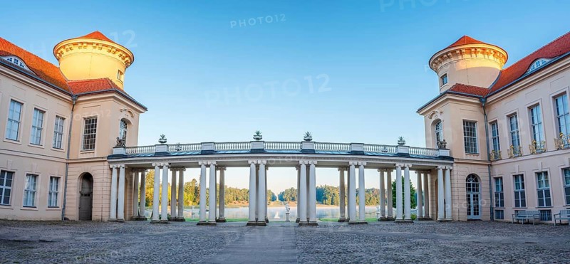 In the inner courtyard of Rheinsberg Castle, view through the arcades of the colonnade to the Lake Grienerick in the morning light, Rheinsberg, Brandenburg, Germany