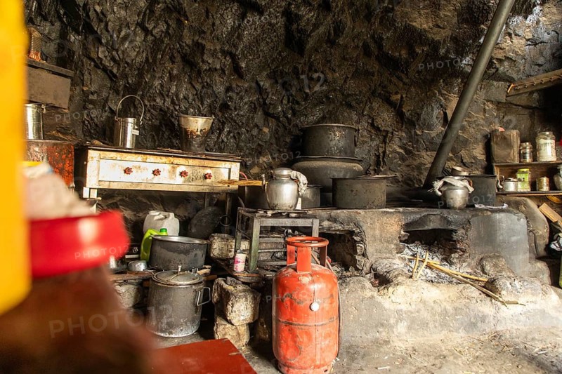 A rustic kitchen within the Phugtal Monastery in Ladakh, showcasing traditional cooking pots and utensils set against an ancient stone wall, highlighting daily monastic life