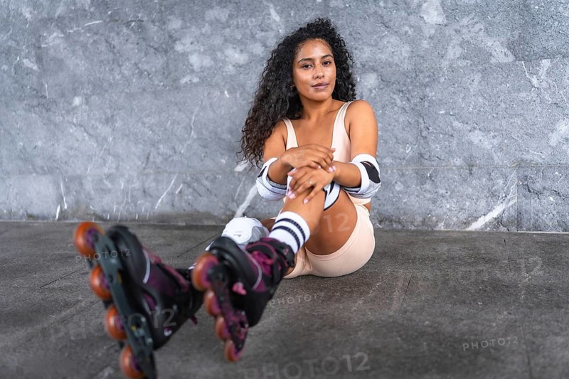 Frontal portrait of a relaxed latin woman wearing in-line skates sitting outdoors smiling