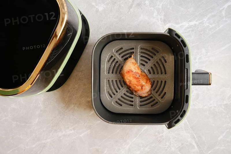 Top view of cooked chicken leg inside modern air fryer basket placed on marble countertop in home kitchen
