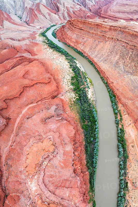 Aerial view of the Rio San Juan curving through dramatic red-and-orange canyon landscapes in Utah, USA, with a thin green line of vegetation along its banks