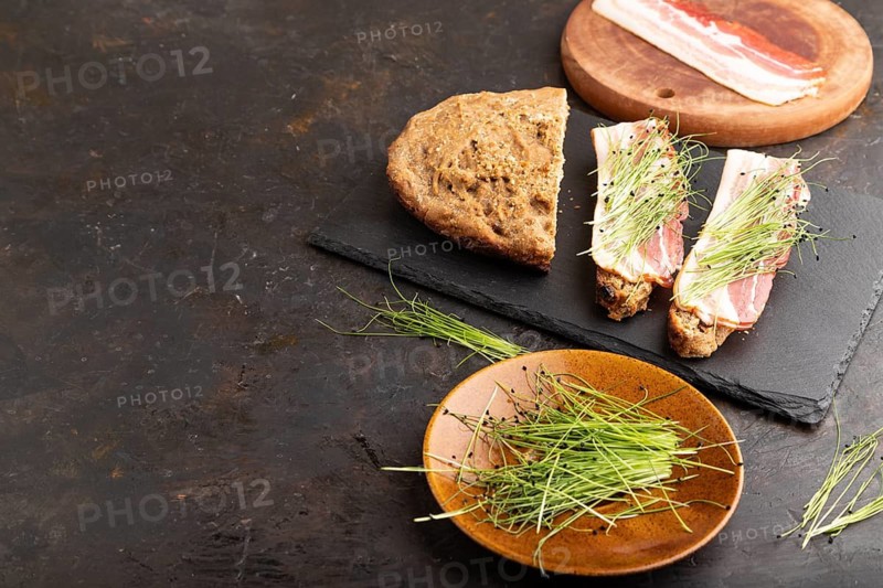 Bread sandwiches with jerky salted meat and lard with onion microgreen on black concrete background. side view, copy space