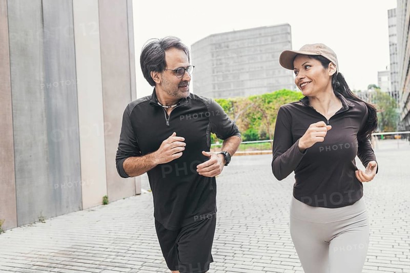 A joyful couple is jogging together on a city street, dressed in sportswear. They enjoy the refreshing morning air as they maintain a healthy lifestyle through outdoor exercise