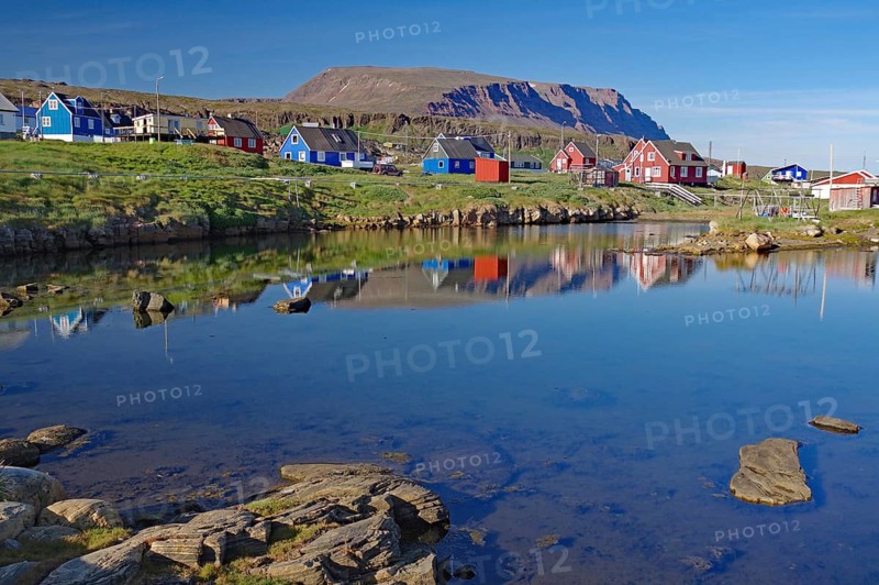 Colourful village reflected in calm water in front of high mountains