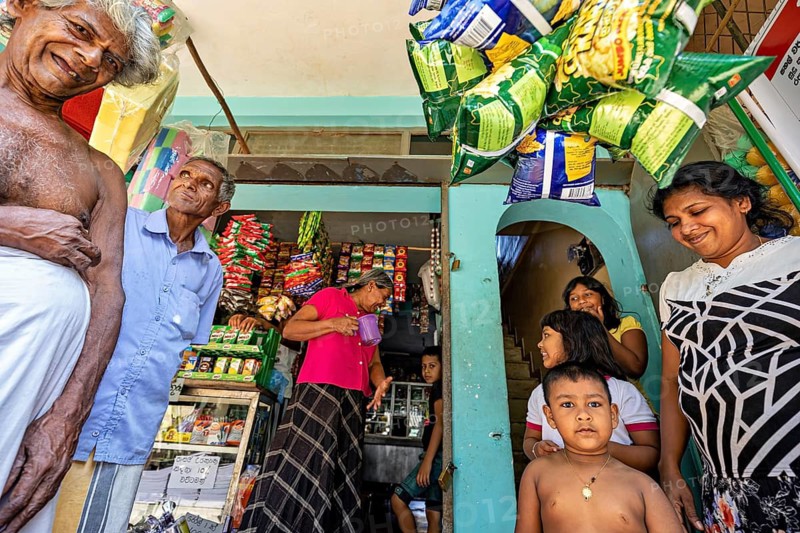 People and children laugh together in front of a small shop filled with goods, a family in Ratnapura in Sri Lanka