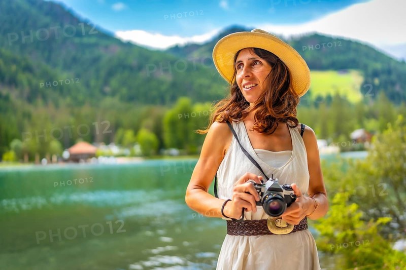 Woman wearing straw hat holding vintage camera enjoying summer holidays at lake dobbiaco in the dolomites, italy