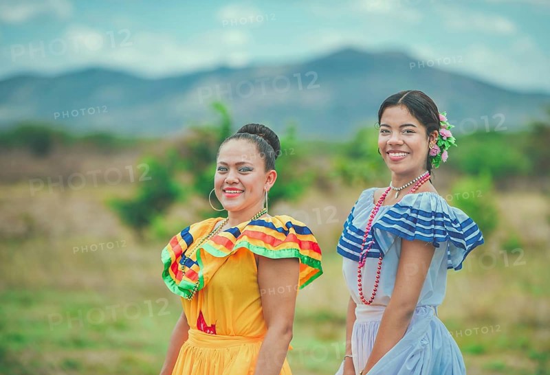 Two smiling Hispanic girls wearing cultural folkloric costumes outdoors. Portrait of two Hispanic women wearing cultural folkloric costume in a field