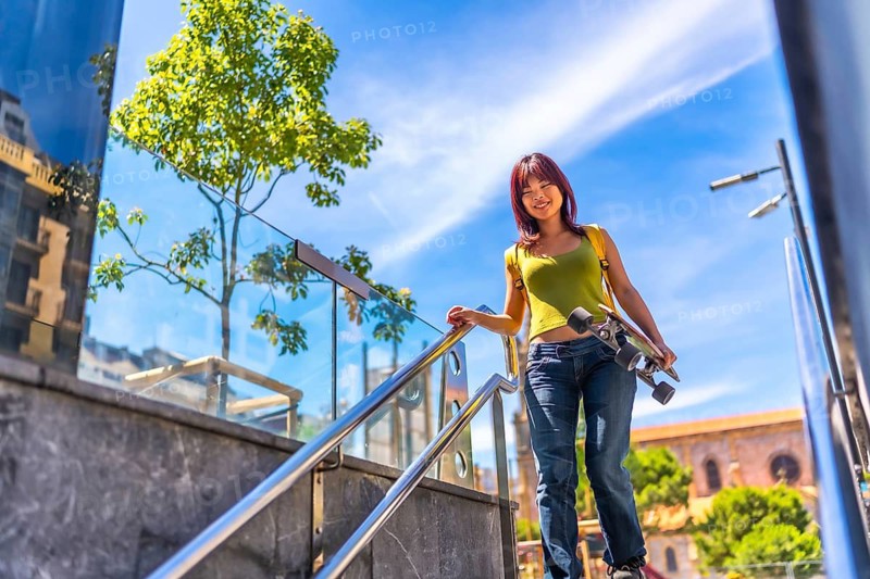 Low angle view photo of a chinese young woman carrying skateboard walking down urban stairs