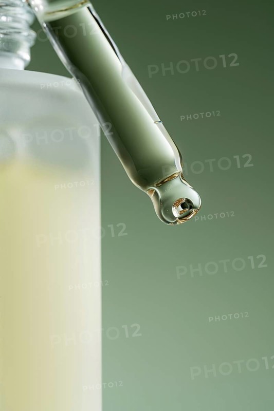 A macro shot of a cosmetic serum dropper dispensing a drop, against a soft green background
