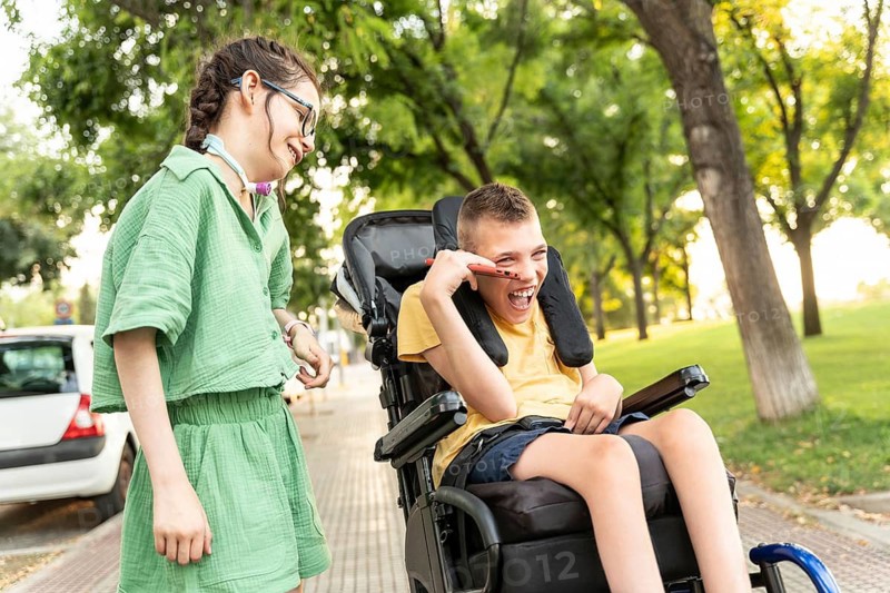A boy with cerebral palsy and a girl with a tracheostomy enjoy a fun day in the park. They share laughter and companionship, highlighting the beauty of friendship and inclusivity