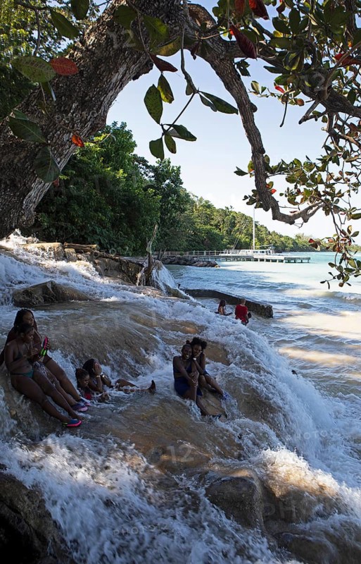 Jamaican woman sit on rocks at Dunn's River Falls or waterfalls at the mouth of the Caribbean Sea, Ochos Rios, Saint Ann Parish, West Indies, Caribbean, Central America