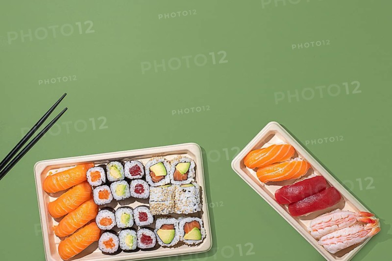 Top down view of assorted sushi in eco friendly trays, set against a modern green backdrop. Perfect for japanese takeout themes