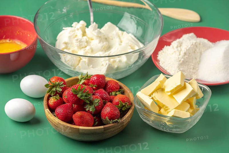 Fresh baking ingredients, including strawberries, butter, sugar and quark, on a green background
